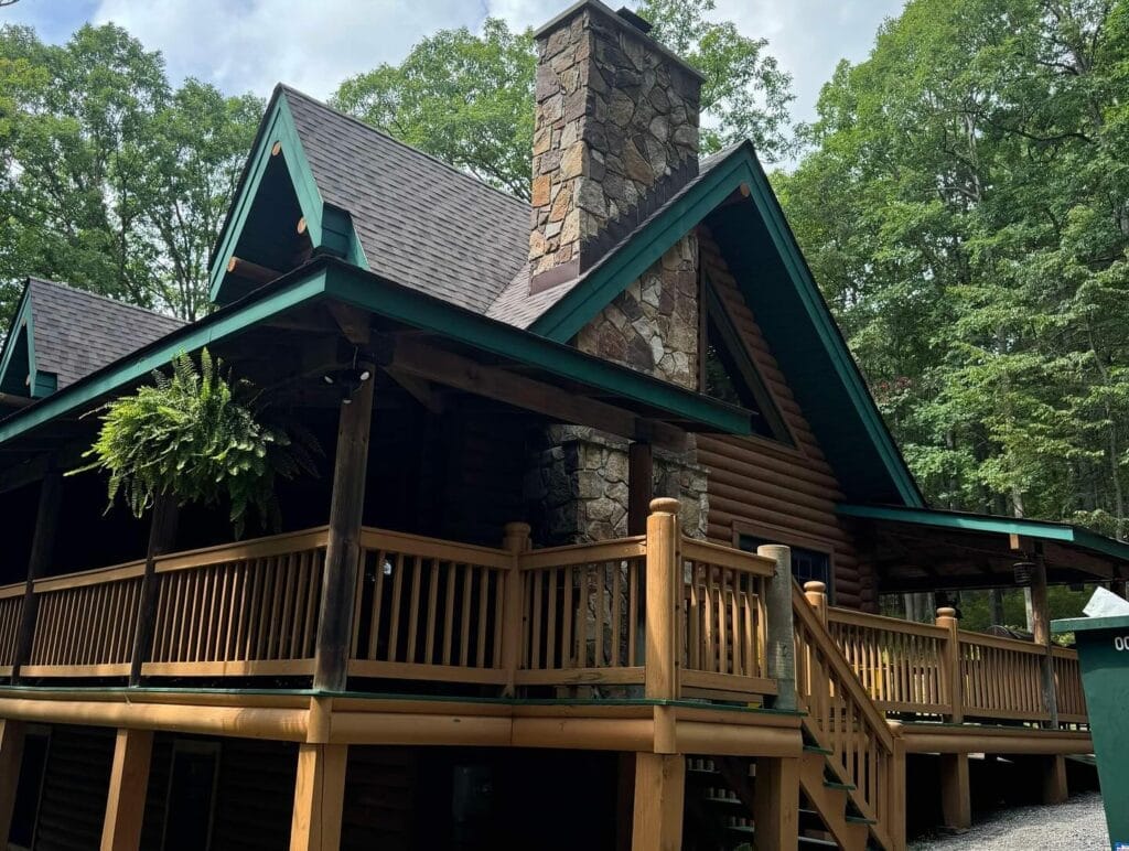 Covered log-home porch with wood railings and stairs under a new shingle roof