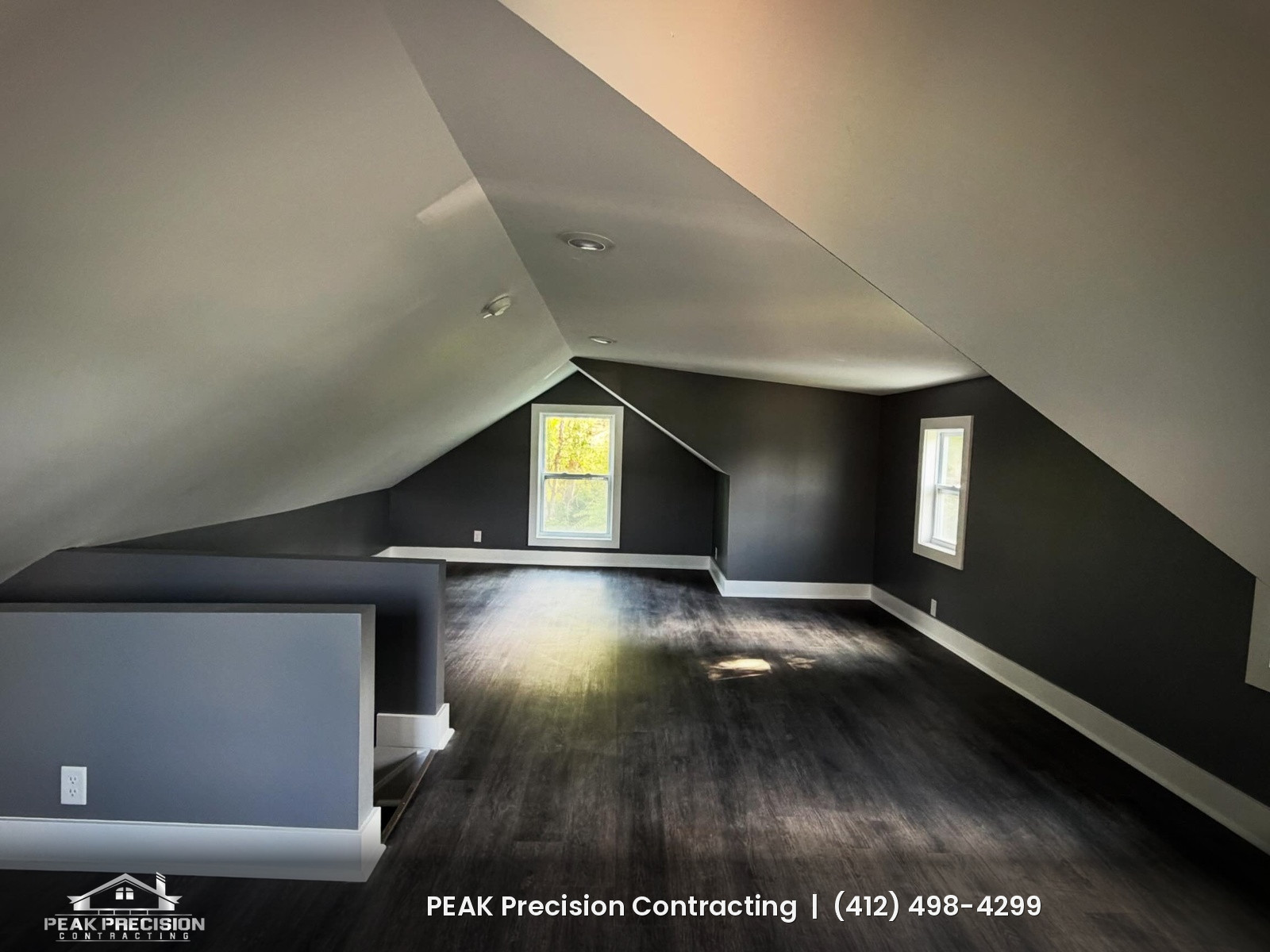 Finished attic room with sloped ceilings, recessed lights, dark walls and new plank flooring, completed by Peak Precision Contracting