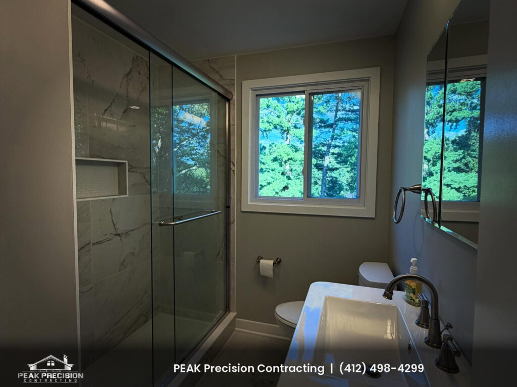 bathroom-remodel-mt-lebanon-pa_bathroom Remodeled bathroom with marble-look tile shower, glass shower doors, recessed tile niche, and white vanity by Peak Precision Contracting