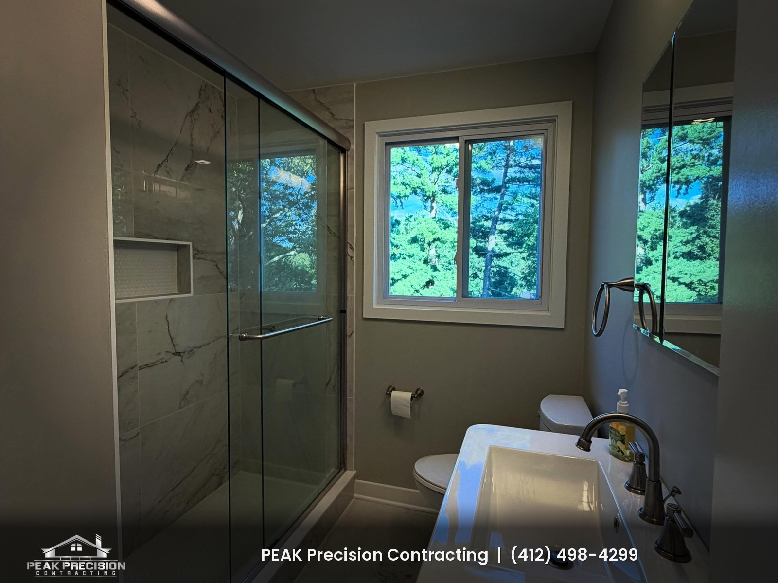 Remodeled bathroom with marble-look tile shower, glass shower doors, recessed tile niche, and white vanity by Peak Precision Contracting