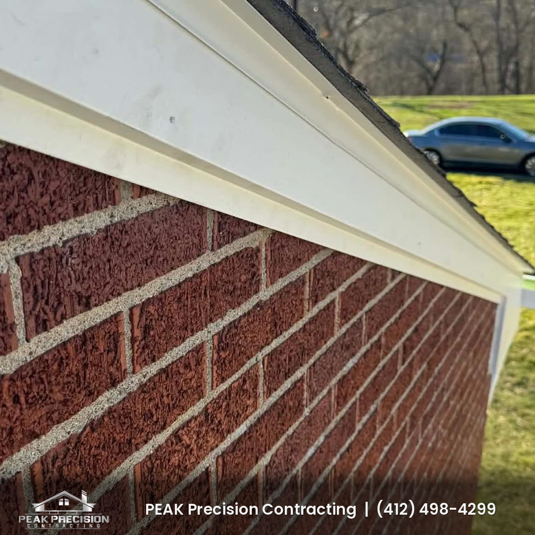 New white seamless gutter along the roof edge of a brick home, installed by Peak Precision Contracting