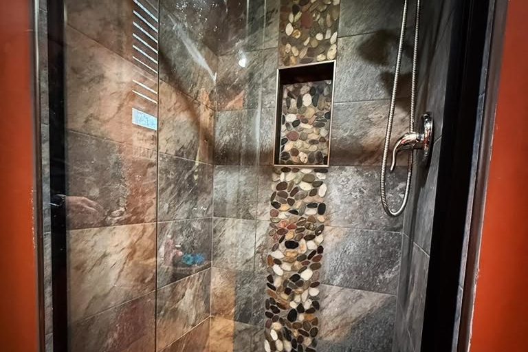 peak-precision-bathroom-remodel-pebble-tile-shower-card-1 Walk-in shower with a river-rock pebble floor, pebble accent strip and niche by Peak Precision Contracting