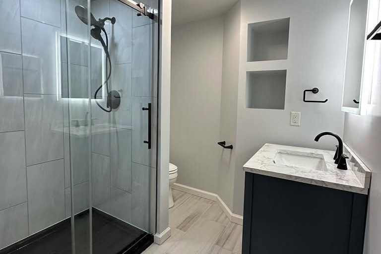 peak-precision-bathroom-remodel-shower-vanity-card-1 Bathroom remodel by Peak Precision Contracting with a sliding glass shower door, navy vanity and wall niches