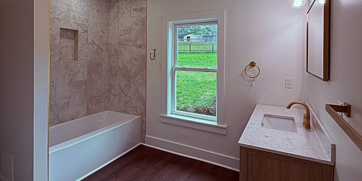 Remodeled bathroom with tub, tile surround and wood vanity by Peak Precision Contracting