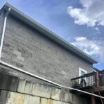 peak-precision-gutter-downspout-installation-1 White gutter and downspout routed down a block wall and across a retaining wall, installed by Peak Precision Contracting