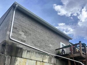 White gutter and downspout routed down a block wall and across a retaining wall, installed by Peak Precision Contracting