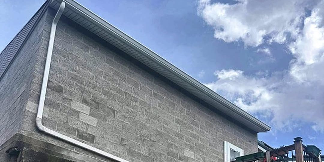 White gutter and downspout along the roof edge of a block building, gutter work by Peak Precision Contracting