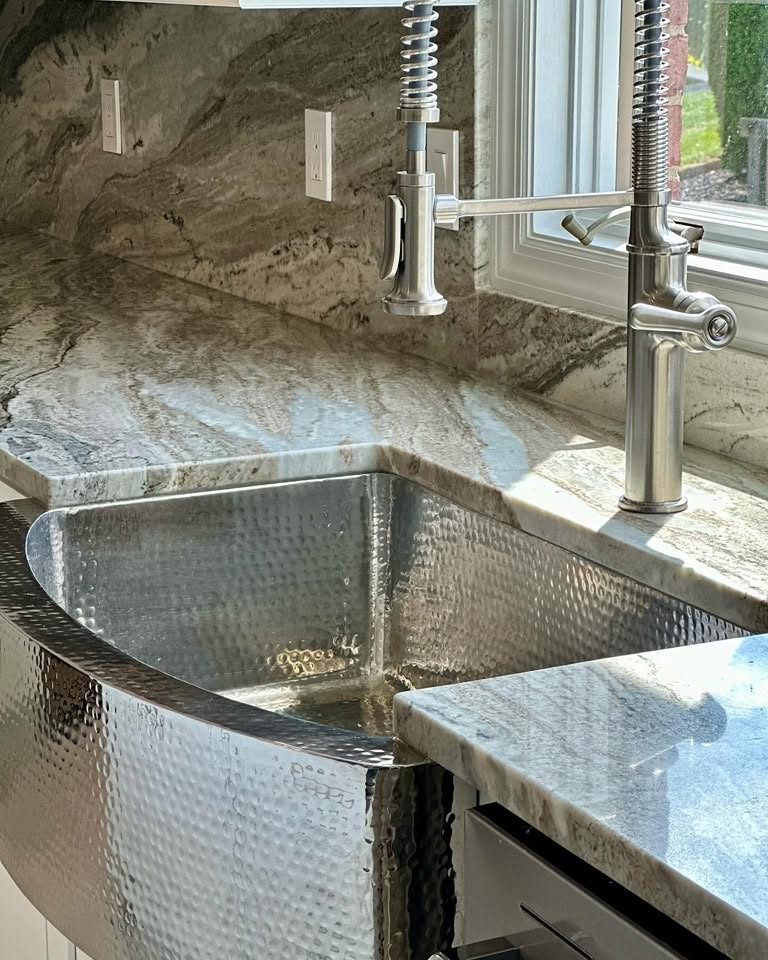 Hammered stainless farmhouse sink with stone countertop and pull-down faucet in a Peak Precision Contracting kitchen remodel