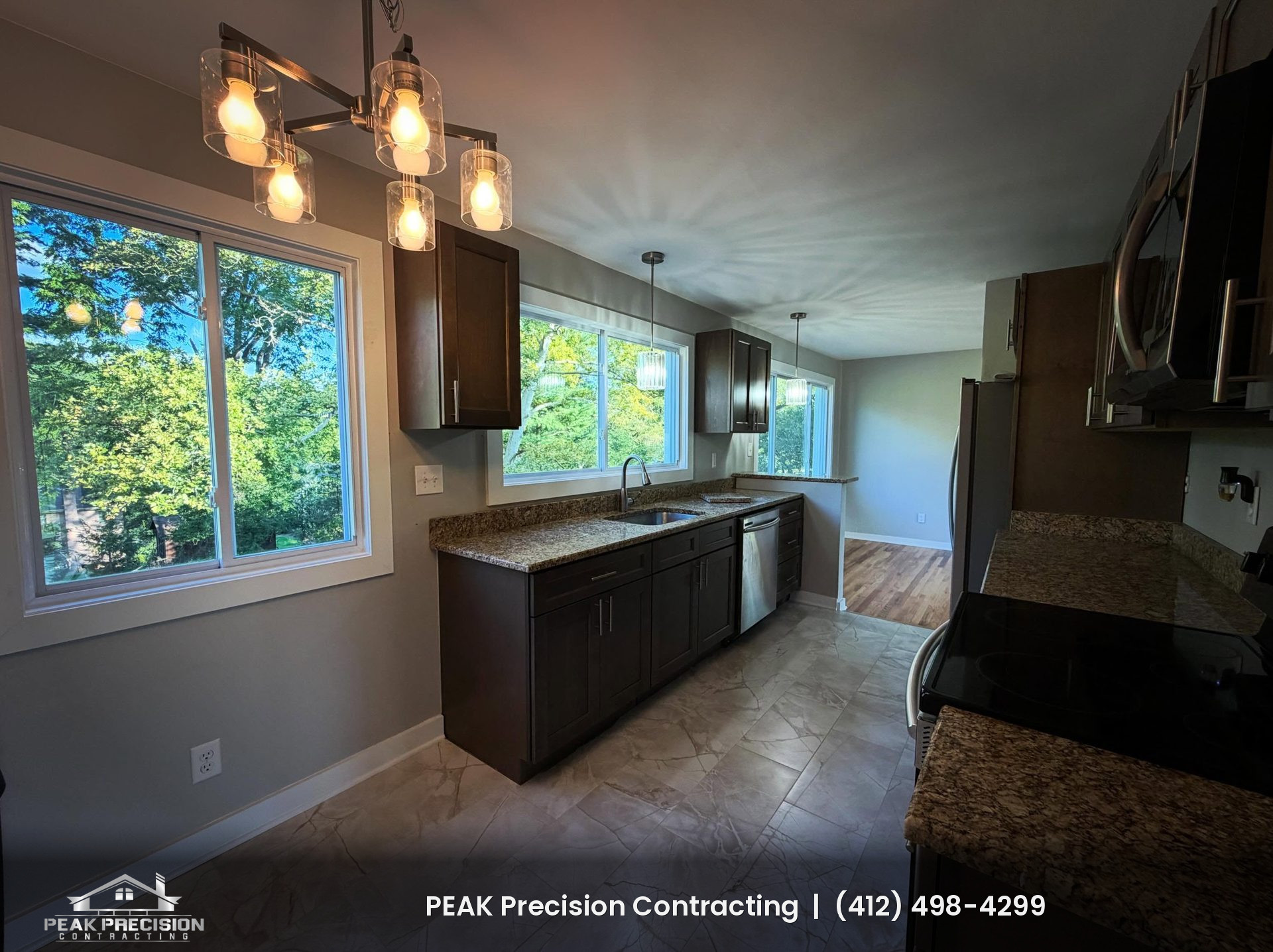 Remodeled kitchen with dark wood cabinets, granite countertops, tile flooring and a sink on an exterior wall, by Peak Precision Contracting
