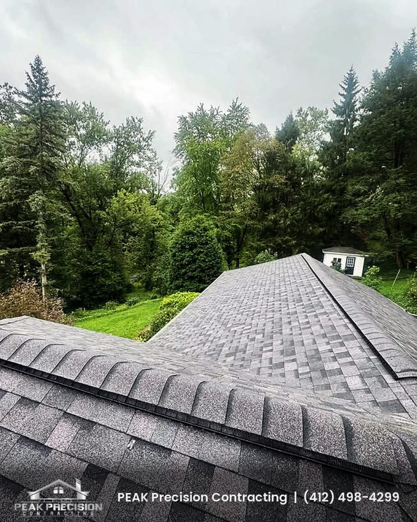 Ridge vent running along the peak of a new gray architectural shingle roof with a wooded backdrop, installed by Peak Precision Contracting