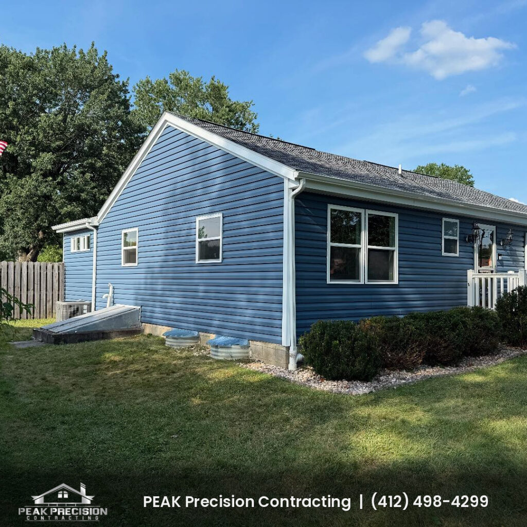 Single-story home with new blue vinyl siding, white trim and corner posts, and white gutters and downspouts, completed by Peak Precision Contracting