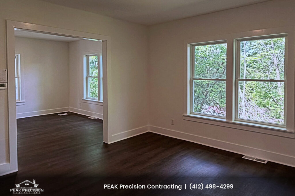 Renovated living room with dark wood-look flooring, white trim and freshly painted walls, completed by Peak Precision Contracting