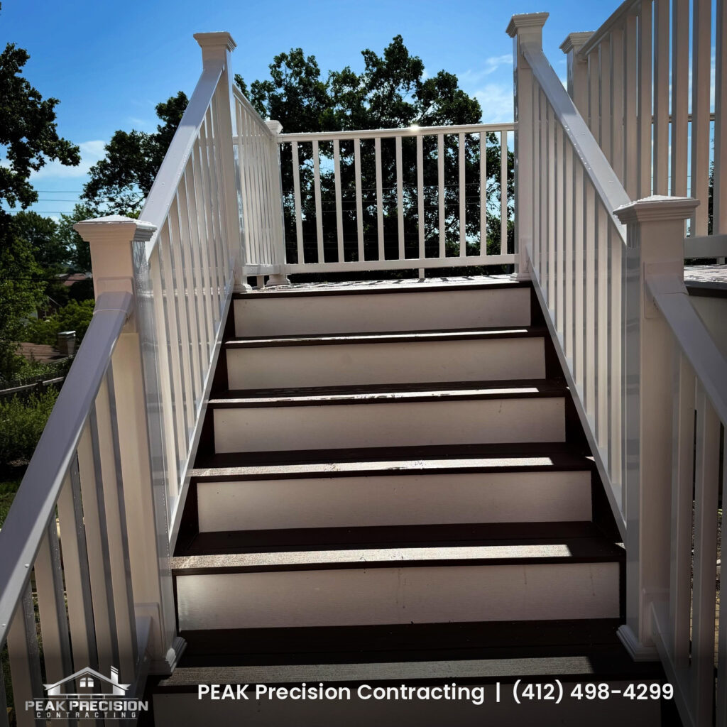 Deck stairs with dark treads and white railings leading up to an elevated deck, built by Peak Precision Contracting