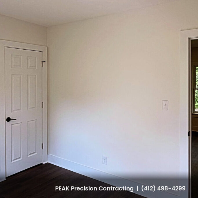Renovated bedroom with new six-panel white doors, white trim, fresh paint and dark wood-look flooring, completed by Peak Precision Contracting