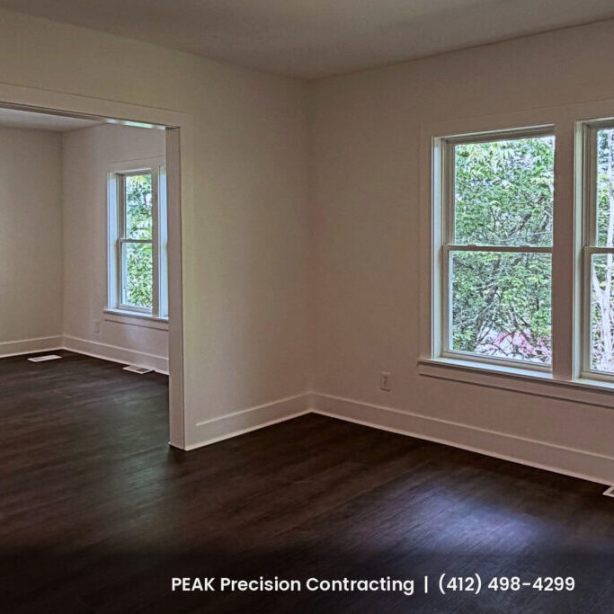 Renovated living room with dark wood-look flooring, white trim and freshly painted walls, completed by Peak Precision Contracting